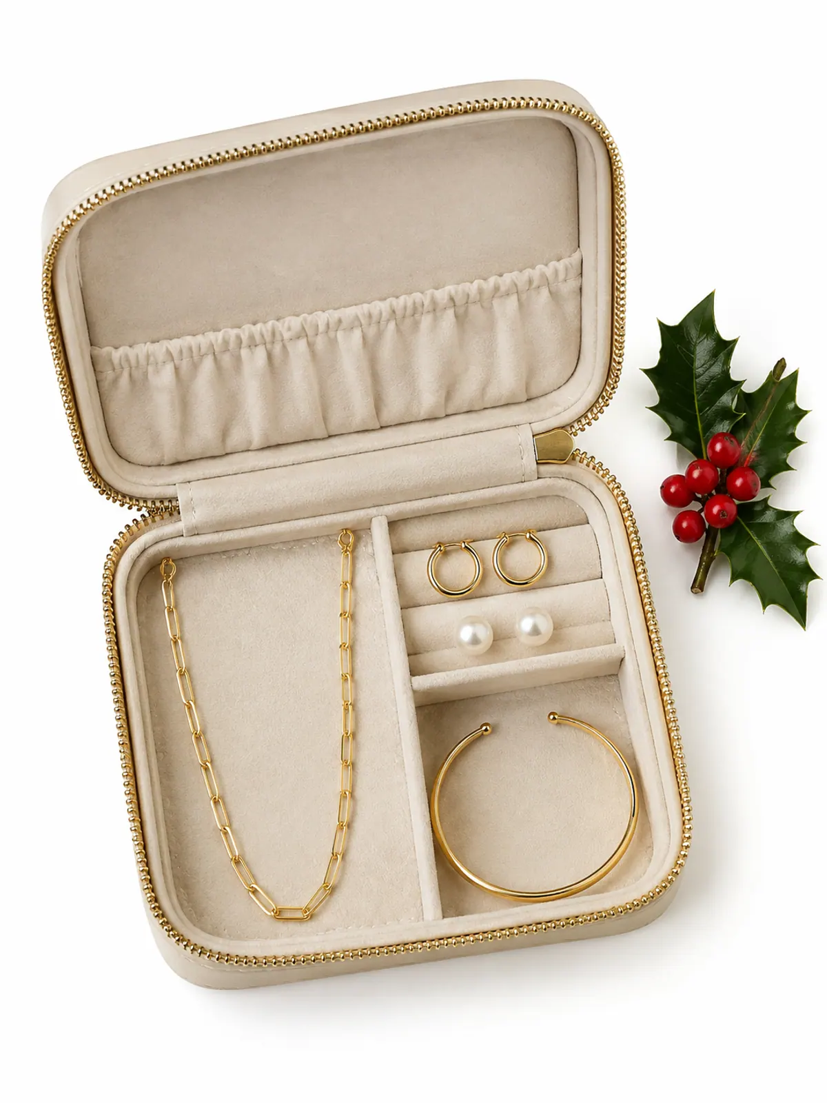 Jewelry Christmas gifts for women over 50: small gold hoops, pearl studs, a gold paperclip chain and a gold cuff in a cream leather travel jewelry case on a walnut dresser