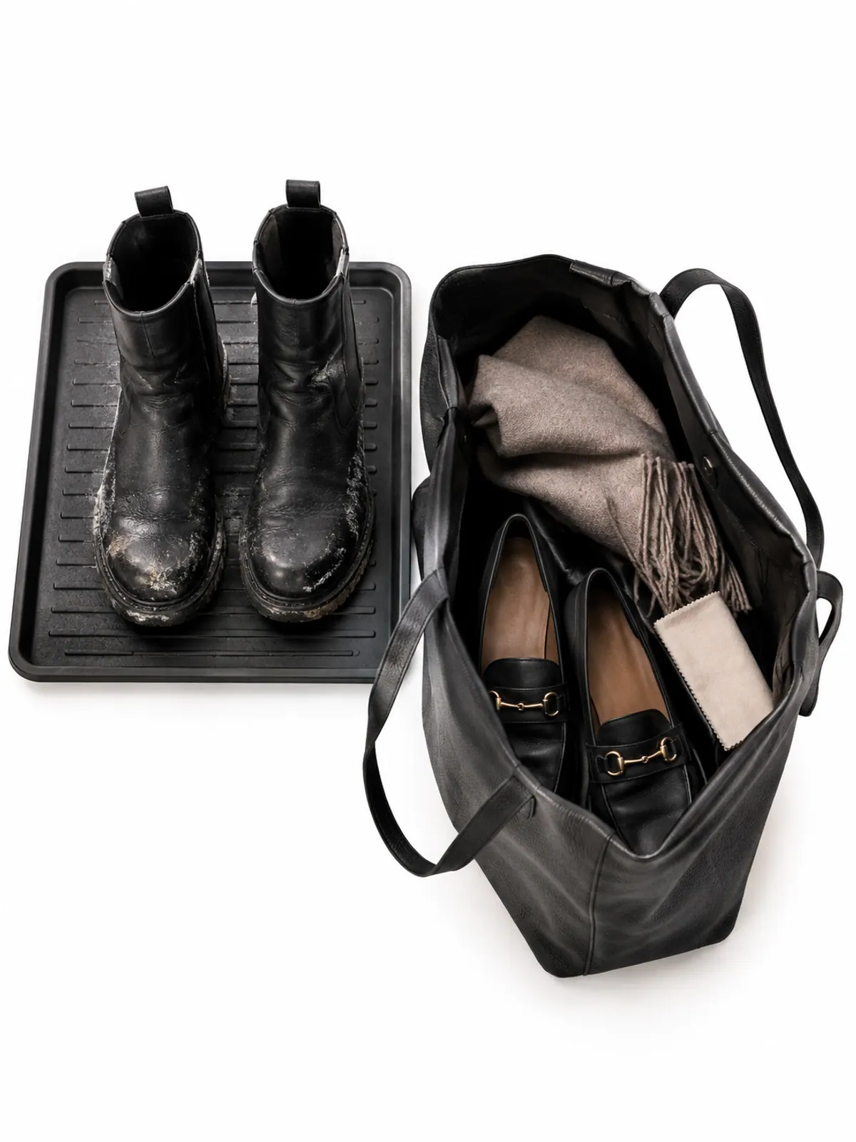 Winter commute shoe swap: black waterproof boots on a rubber tray under an office desk next to an open tote holding black loafers, a cashmere scarf and a shoe cloth